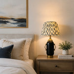 Charger l'image dans la visionneuse de la galerie, Matte black floral table lamp glowing on a bedroom nightstand