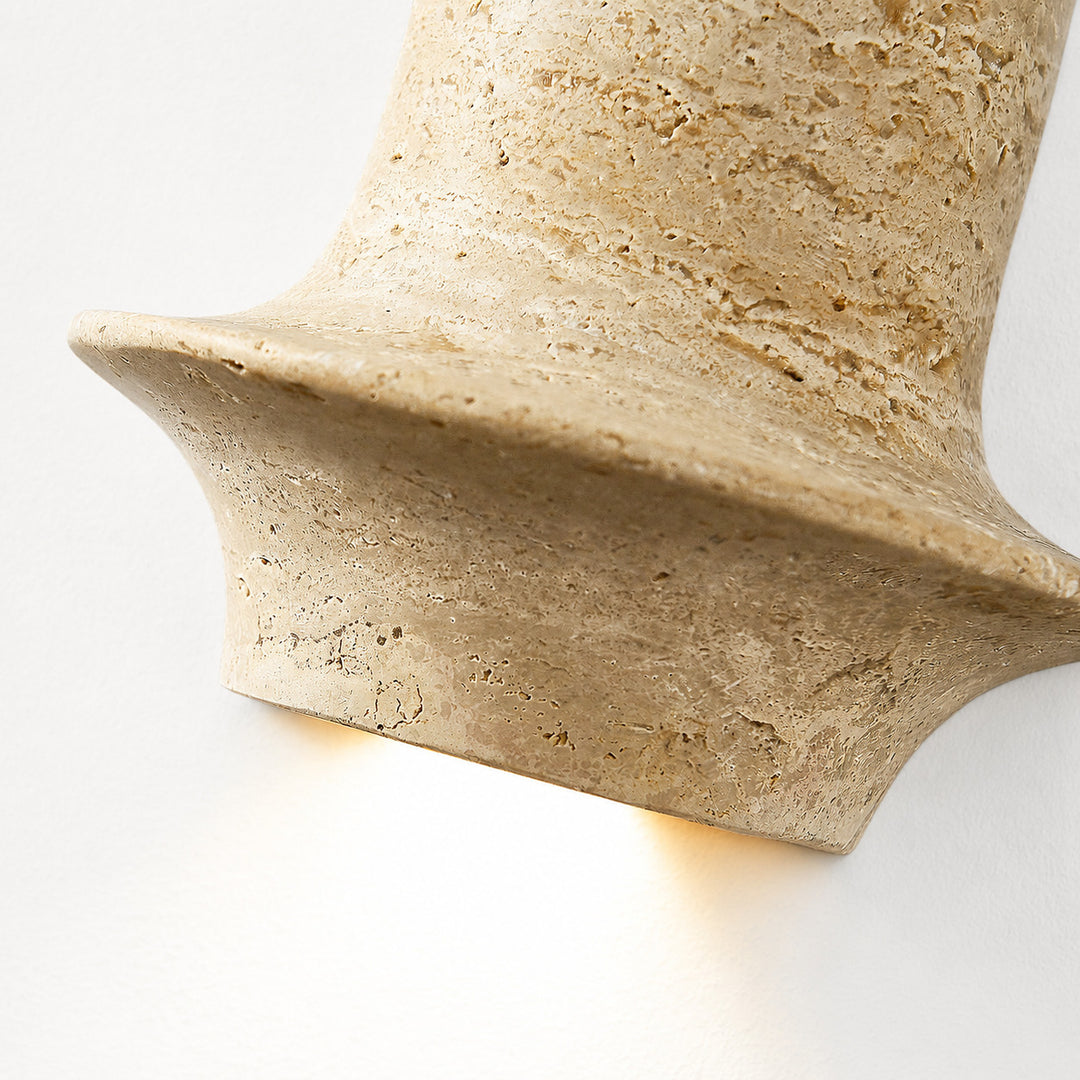 Lit close view of travertine wall lamp showing warm downward glow and honed stone edge