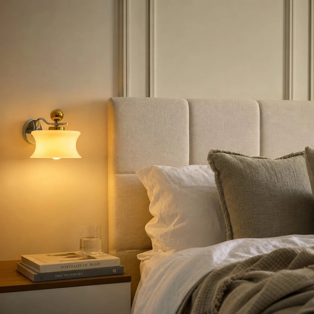 Cream glass wall lamp casting warm bedside light