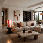 Load image into Gallery viewer, Red and cream striped woven table lamp glowing in a living room