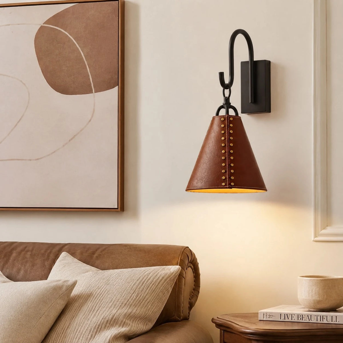 Leather cone wall sconce casting warm light beside a bed and framed wall art