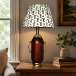 Charger l'image dans la visionneuse de la galerie, Deep brown floral table lamp glowing beside framed wall art