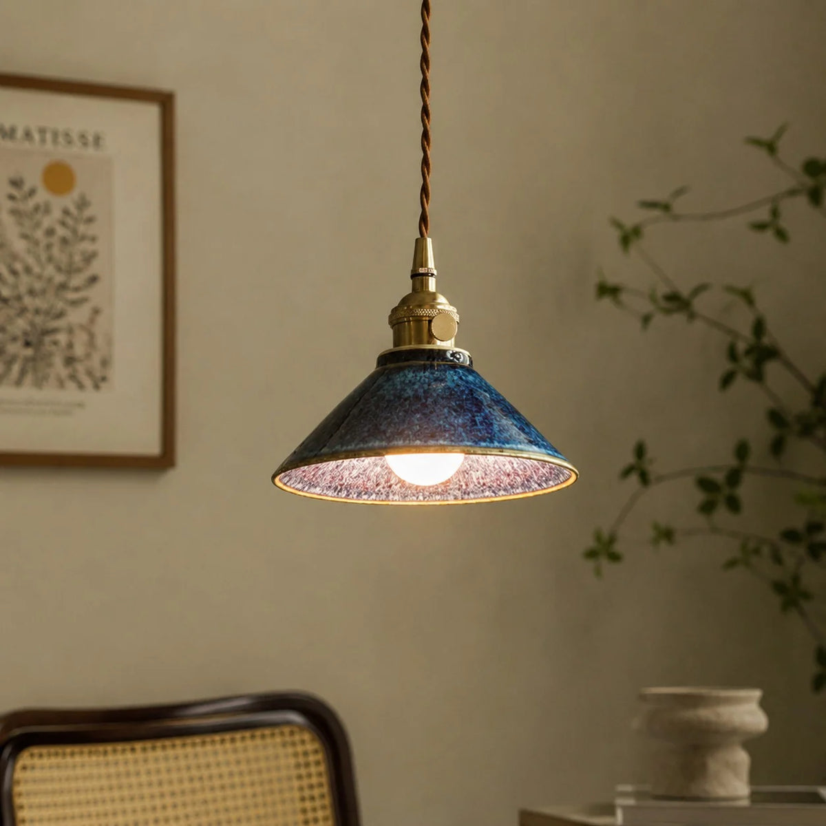 Blue ceramic pendant light beside a woven chair and wall art