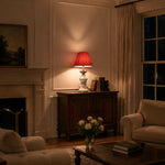Afbeelding laden in galerijweergave, Red bedside table lamp glowing in an evening room