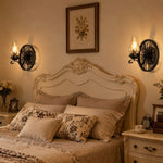 Załaduj obraz do przeglądarki galerii, Pair of black wagon wheel wall sconces beside a classic bedroom headboard